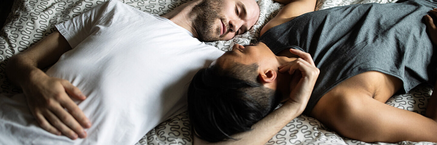 Ein homosexuelles Paar kuschelt im Bett und redet über Erektionsprobleme.