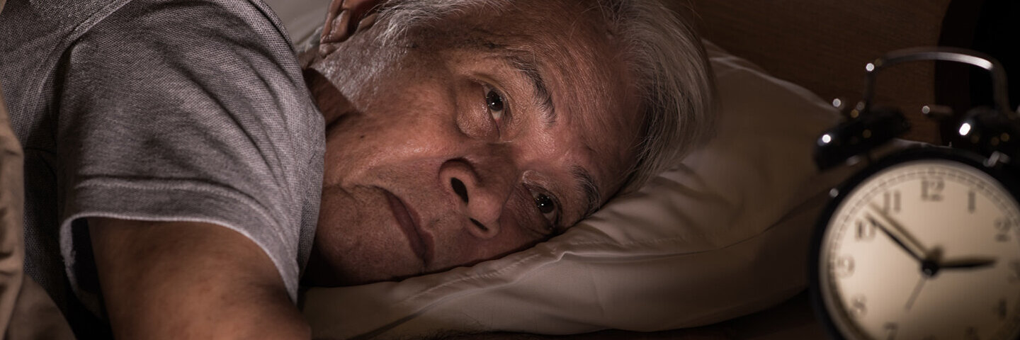 Älterer Mann liegt wach im Bett, weil er nicht schlafen kann.