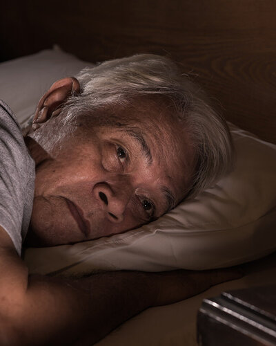 Älterer Mann liegt wach im Bett, weil er nicht schlafen kann.