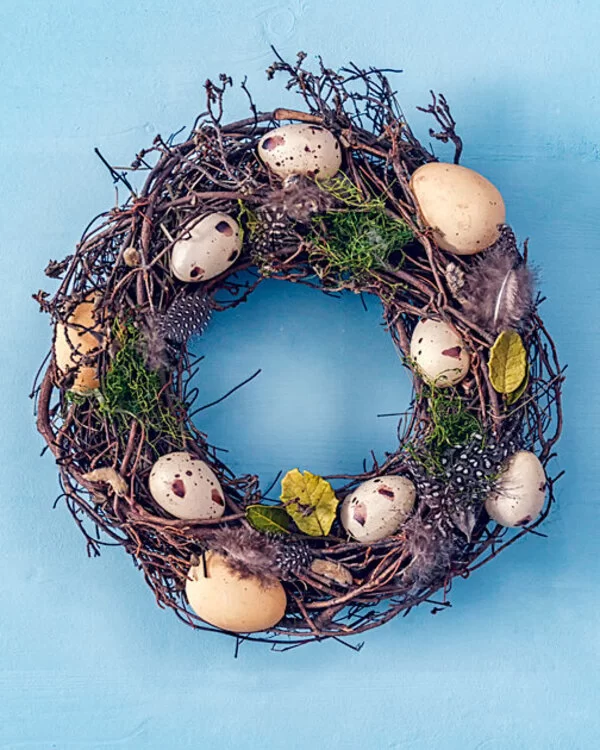 Ein Osterkranz aus Naturmaterialien ist mit Wachteleiern, Hühnereiern und Federn verziert.