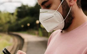 Junger Mann trägt FFP2-Maske und steht am Bahnhof.