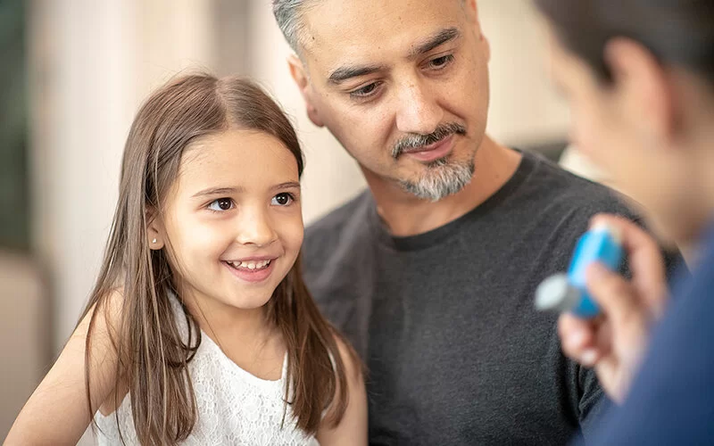 Vater und Kind erfahren von einem Fachmann, wie sie Asthmaspray anwenden können.