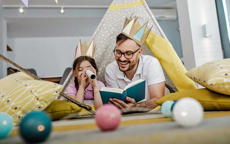 Ein Vater liest seiner Tochter eine Geschichte vor, die eine Küchenpapierrolle als Fernglas benutzt.