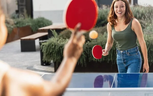 Zwei junge Frauen in Freizeitkleidung spielen Tischtennis in einer öffentlichen Grünanlage.
