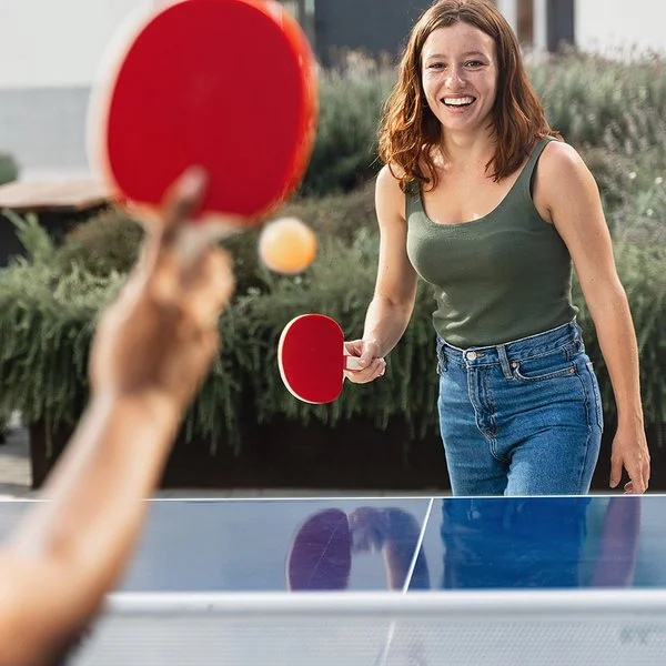 Zwei junge Frauen in Freizeitkleidung spielen Tischtennis in einer öffentlichen Grünanlage.