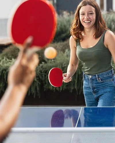Zwei junge Frauen in Freizeitkleidung spielen Tischtennis in einer öffentlichen Grünanlage.