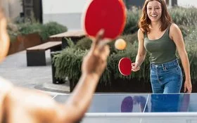 Zwei junge Frauen in Freizeitkleidung spielen Tischtennis in einer öffentlichen Grünanlage.