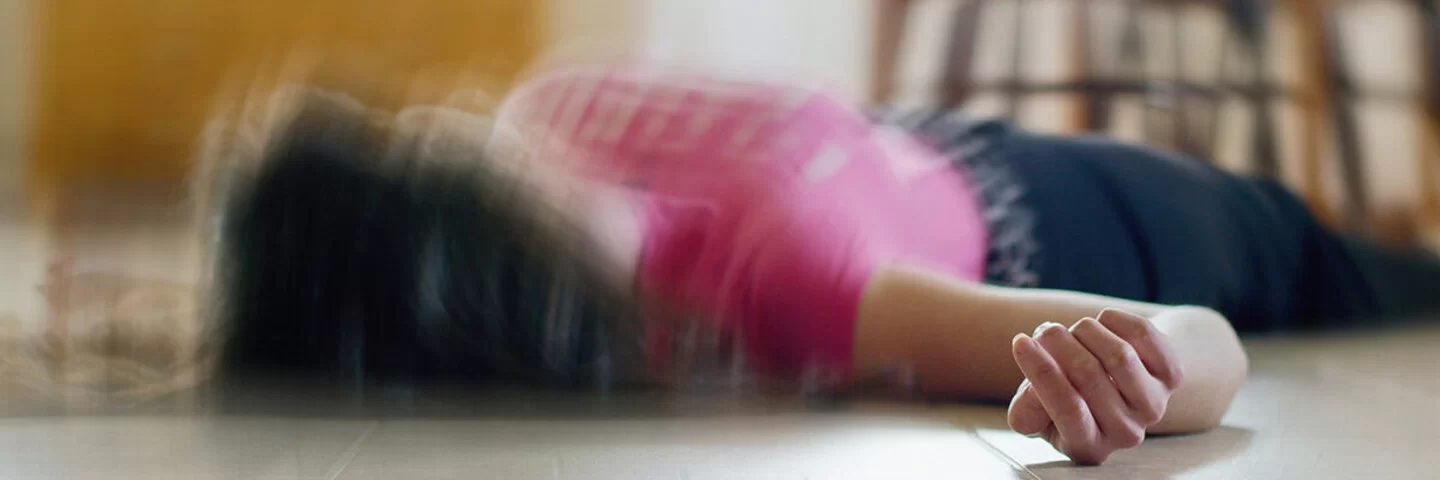 Eine Frau liegt mit einem epileptischen Anfall auf dem Boden