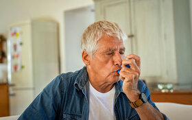 Ein Mann, der unter Asthma leidet, inhaliert mit seinem Asthma-Spray.
