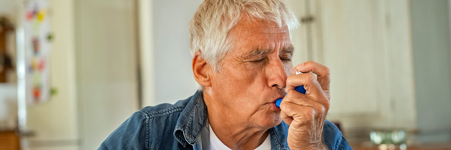 Ein Mann, der unter Asthma leidet, inhaliert mit seinem Asthma-Spray.