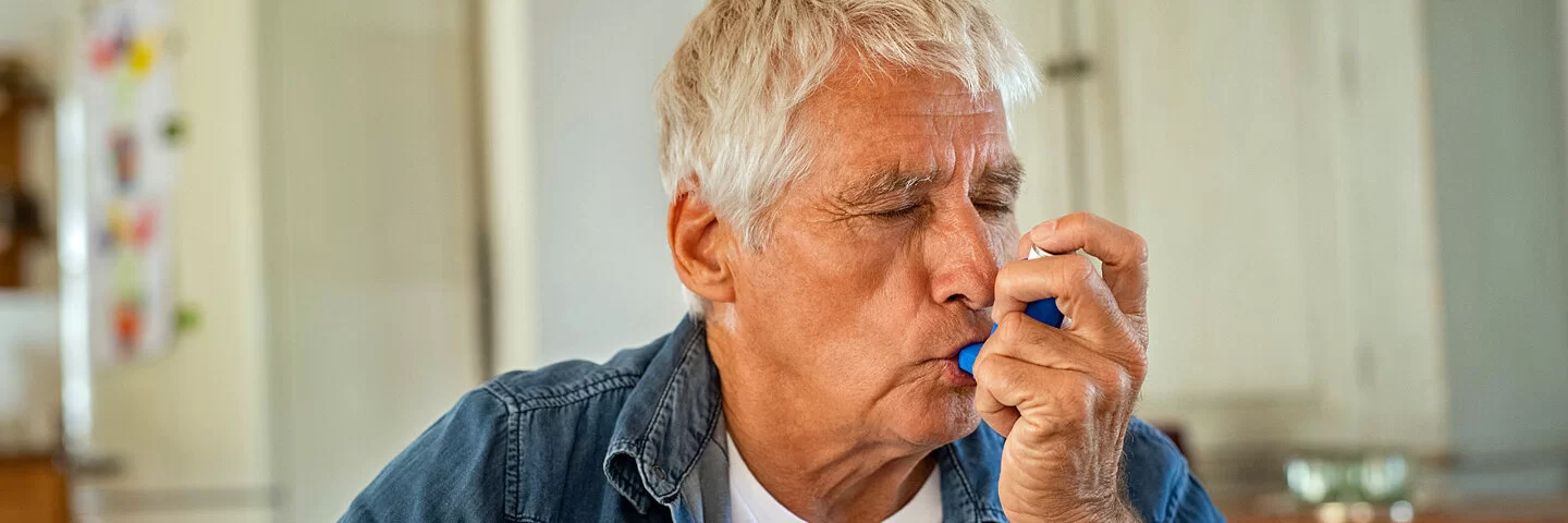 Ein Mann, der unter Asthma leidet, inhaliert mit seinem Asthma-Spray.