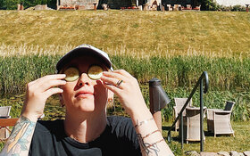 Evelyn Weigert sitzt mit Gurken auf den Augen auf einer Wiese