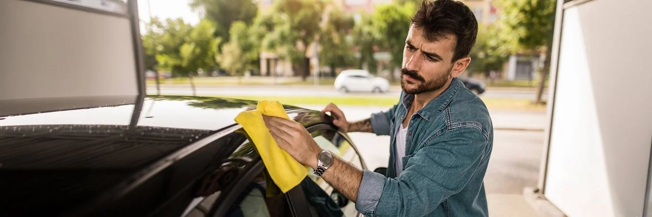 Ein Mann wäscht sein Auto von Hand und guckt dabei kritisch.