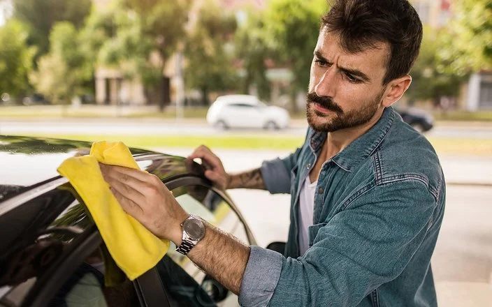 Ein Mann wäscht sein Auto von Hand und guckt dabei kritisch.