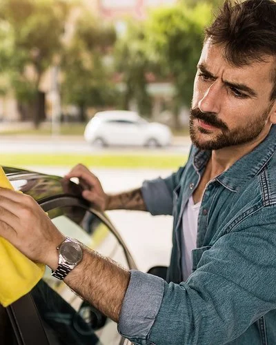 Ein Mann wäscht sein Auto von Hand und guckt dabei kritisch.