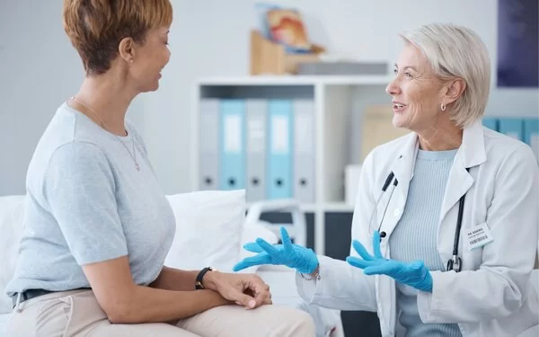 Eine Mastopathie-Patientin sitzt auf einer Untersuchungsliege und lässt sich von einer älteren Ärztin beraten.