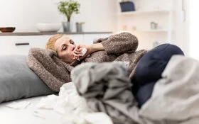 Eine Frau mit einer akuten Bronchitis liegt auf dem Sofa und hustet.