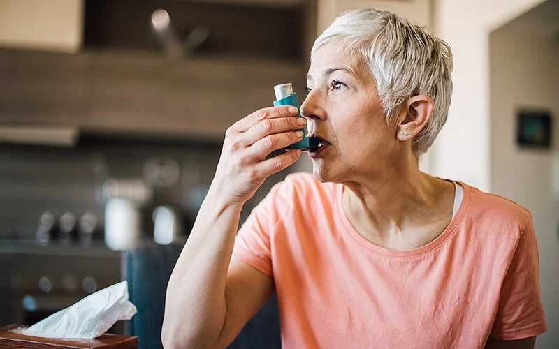 Eine ältere Frau mit chronisch-obstruktiver Bronchitis inhaliert ein bronchienerweiterndes Spray.