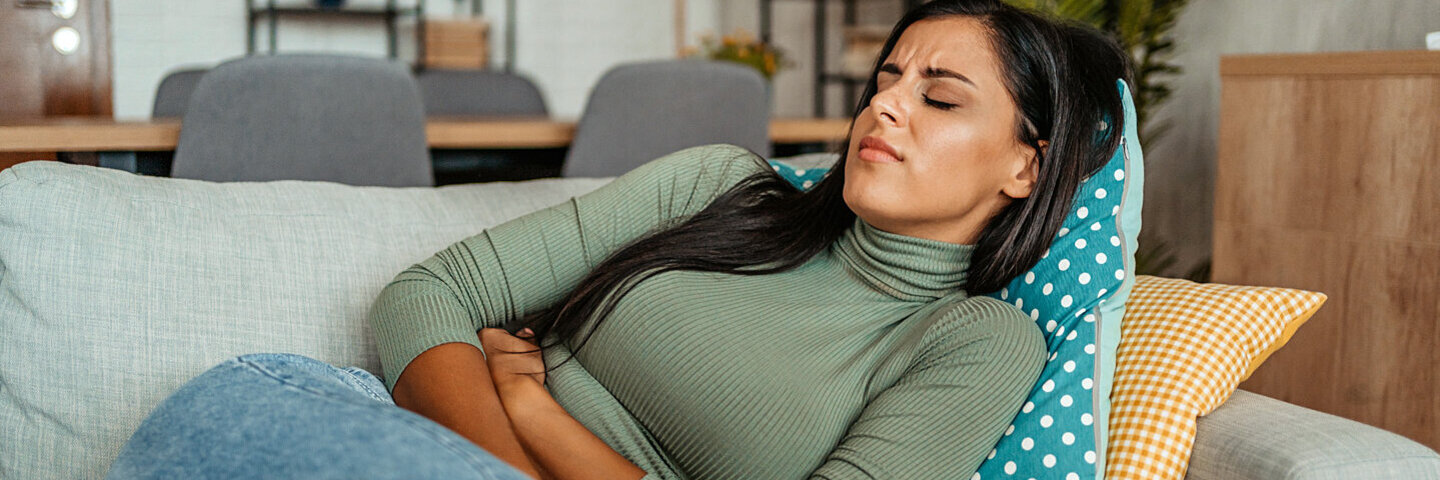 Eine Frau mit Reizdarmsyndrom liegt auf einem Sofa und leidet unter Verdauungsproblemen.