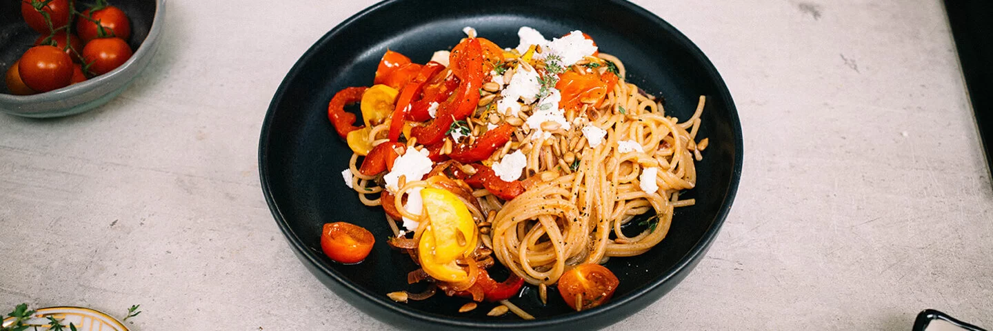 Bunte Sommerpasta mit Gemüse nach einem Rezept von Felicitas Then, angerichtet auf einem schwarzen Teller, garniert mit Feta und Sonnenblumenkernen.