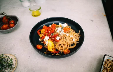 Bunte Sommerpasta mit Gemüse nach einem Rezept von Felicitas Then, angerichtet auf einem schwarzen Teller, garniert mit Feta und Sonnenblumenkernen.