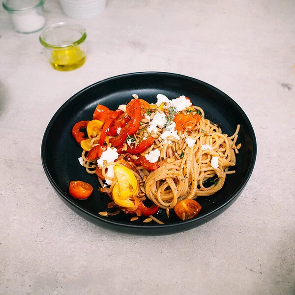 Bunte Sommerpasta mit Gemüse nach einem Rezept von Felicitas Then, angerichtet auf einem schwarzen Teller, garniert mit Feta und Sonnenblumenkernen.