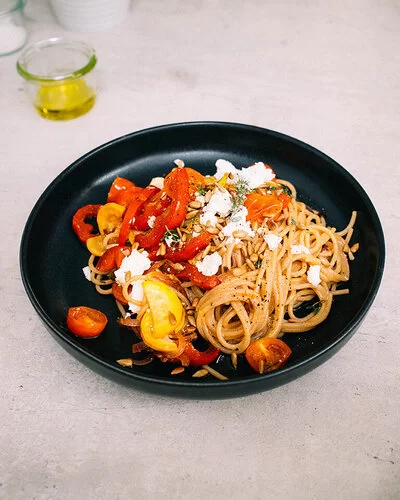 Bunte Sommerpasta mit Gemüse nach einem Rezept von Felicitas Then, angerichtet auf einem schwarzen Teller, garniert mit Feta und Sonnenblumenkernen.