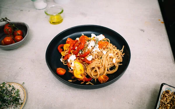 Bunte Sommerpasta mit Gemüse nach einem Rezept von Felicitas Then, angerichtet auf einem schwarzen Teller, garniert mit Feta und Sonnenblumenkernen.