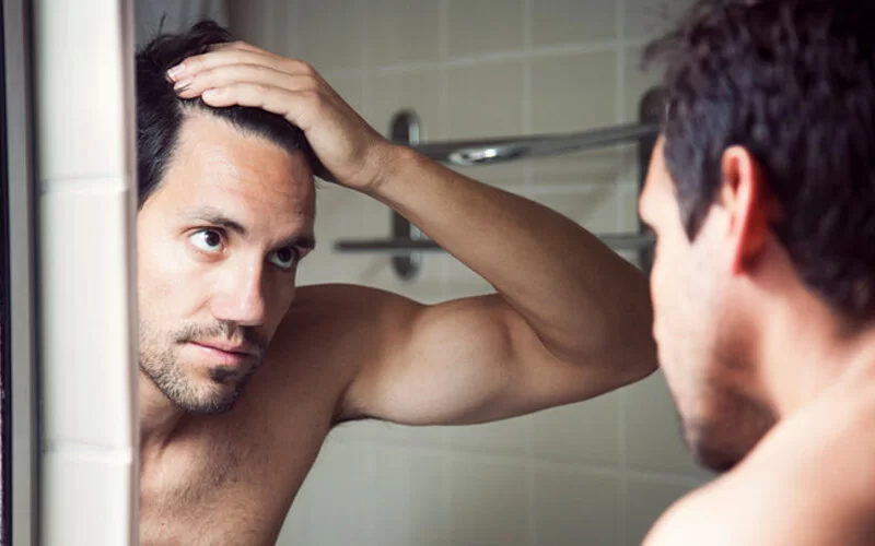 Ein Mann überprüft vor dem Spiegel seinen Haarausfall.