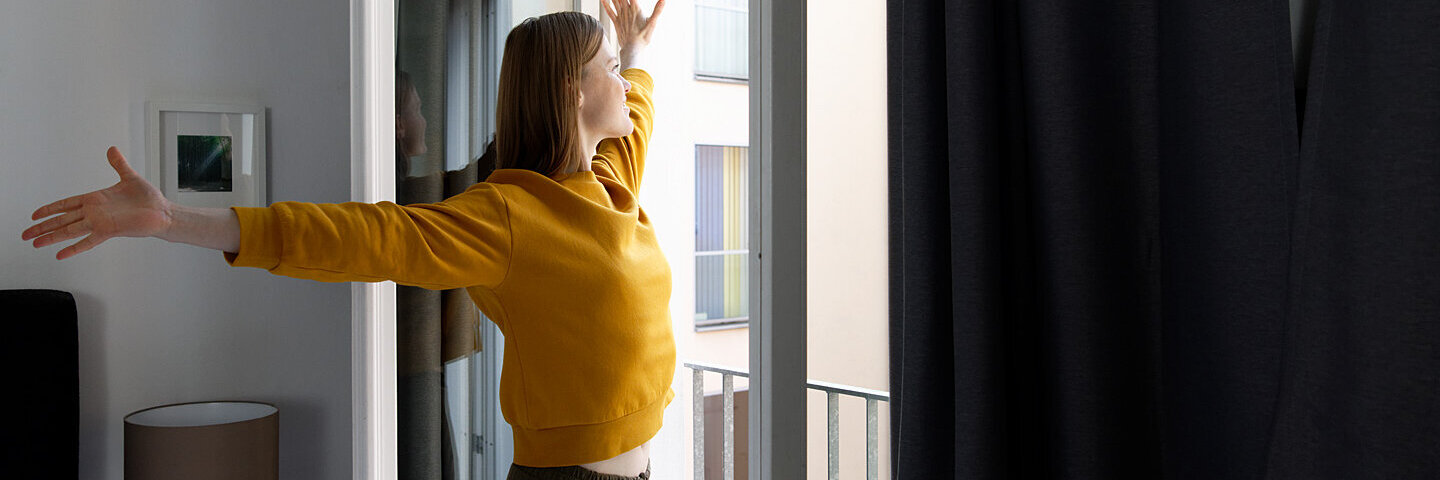 Eine junge Frau steht voller Energie vor der offenen Balkontür.