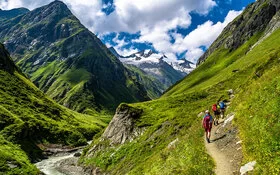 An einem Sommertag macht sich eine dreiköpfige Wandergruppe aus einem Tal auf den Weg zum Gipfel.