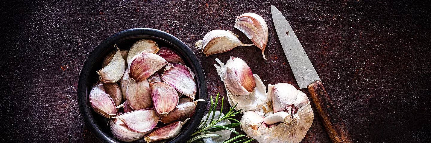 Kann eine Knoblauch-Unverträglichkeit auslösen: Neben einer Knoblauchknolle liegen Knoblauchzehen in einer schwarzen Schale.