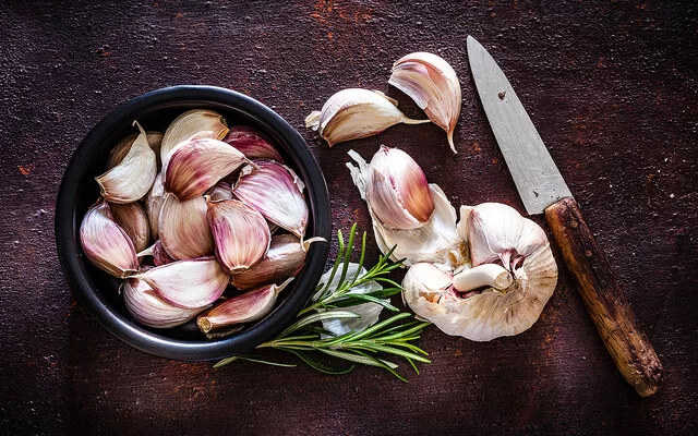 Kann eine Knoblauch-Unverträglichkeit auslösen: Neben einer Knoblauchknolle liegen Knoblauchzehen in einer schwarzen Schale.