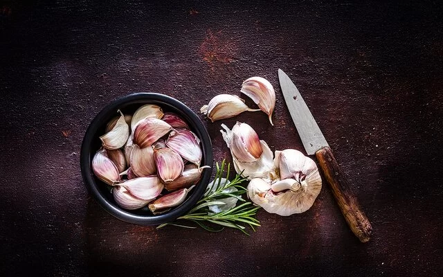 Kann eine Knoblauch-Unverträglichkeit auslösen: Neben einer Knoblauchknolle liegen Knoblauchzehen in einer schwarzen Schale.