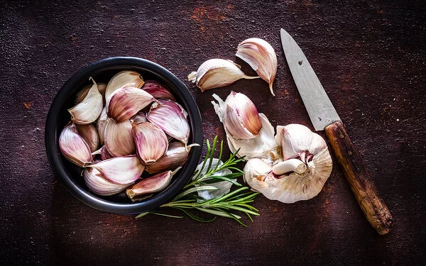 Kann eine Knoblauch-Unverträglichkeit auslösen: Neben einer Knoblauchknolle liegen Knoblauchzehen in einer schwarzen Schale.