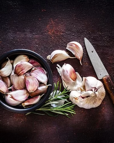 Kann eine Knoblauch-Unverträglichkeit auslösen: Neben einer Knoblauchknolle liegen Knoblauchzehen in einer schwarzen Schale.