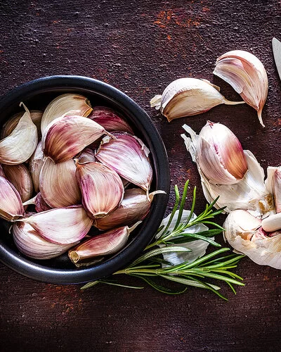 Kann eine Knoblauch-Unverträglichkeit auslösen: Neben einer Knoblauchknolle liegen Knoblauchzehen in einer schwarzen Schale.
