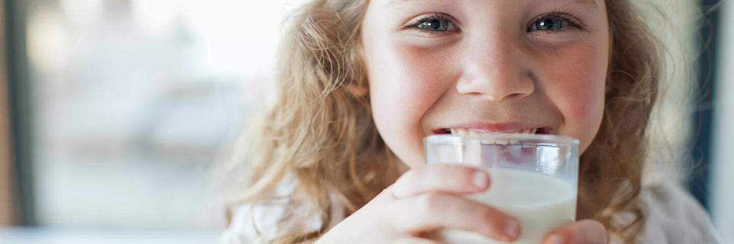 Ein kleines Mädchen trinkt aus einem Glas Milch.