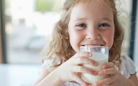 Ein kleines Mädchen trinkt aus einem Glas Milch.