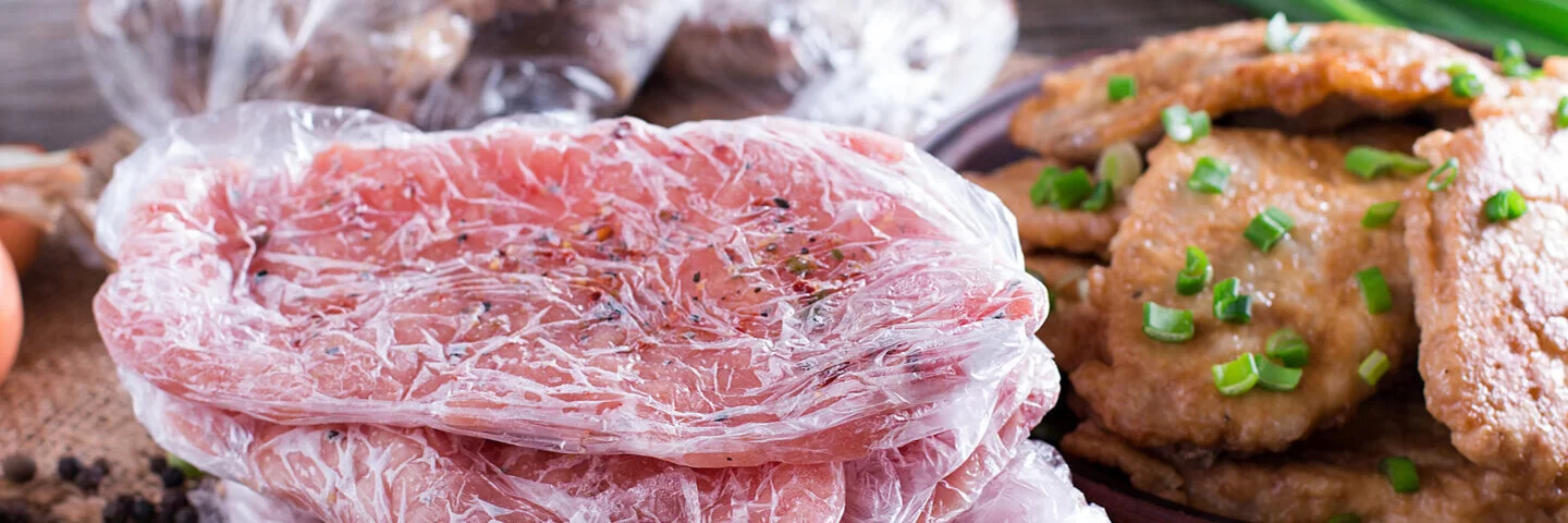 Teilweise gefrorene Fleischscheiben in Plastiktüten neben frischen Zutaten gelagert.