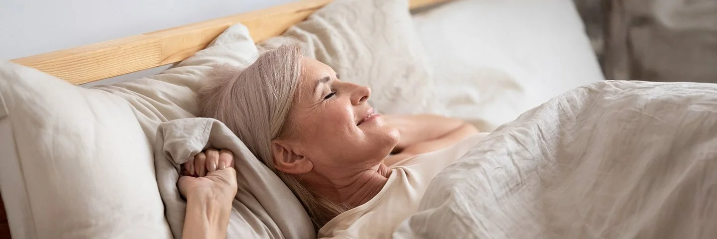 Gesunder Schlaf im Alter: Frau liegt im Bett und genießt den Schlaf.