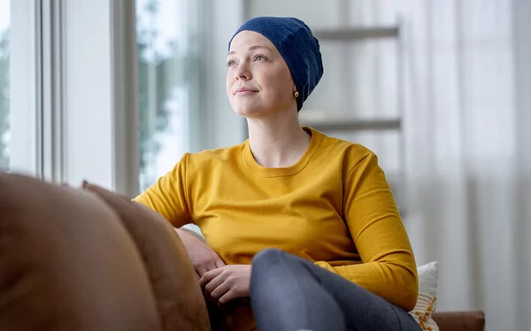 Eine Frau mit einem Tuch um den Kopf schaut vom Sofa aus dem Fenster.
