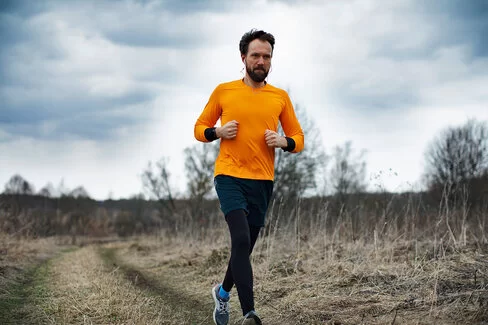 Ein Jogger läuft im Winter auf einem kahlen Feldweg entlang.