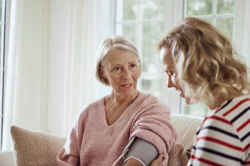 Frau mittleren Alters misst den Blutdruck einer Seniorin.