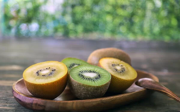 Auf einer Holzschale liegen aufgeschnittene gelbe und grüne Kiwis.
