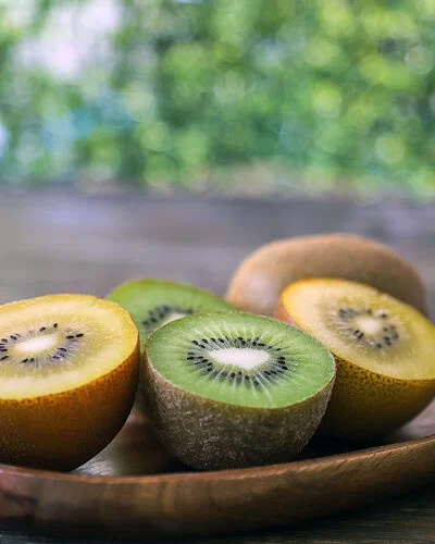 Auf einer Holzschale liegen aufgeschnittene gelbe und grüne Kiwis.