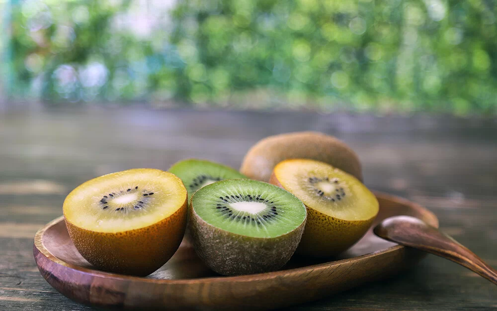 Auf einer Holzschale liegen aufgeschnittene gelbe und grüne Kiwis.