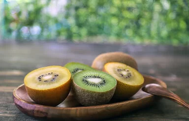 Auf einer Holzschale liegen aufgeschnittene gelbe und grüne Kiwis.