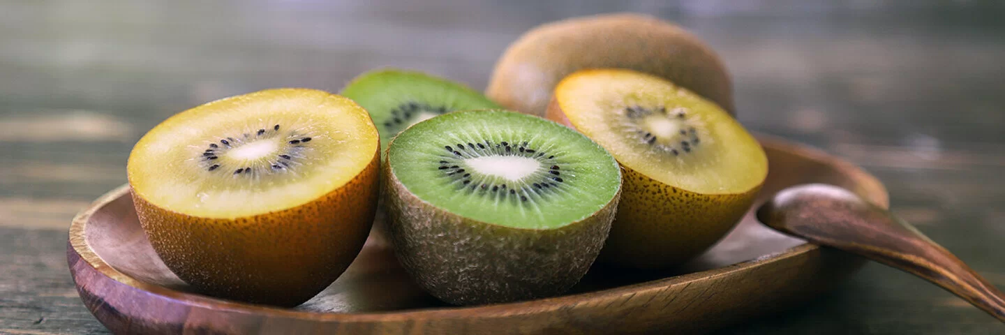 Auf einer Holzschale liegen aufgeschnittene gelbe und grüne Kiwis.