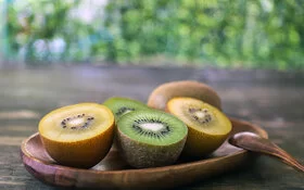 Auf einer Holzschale liegen aufgeschnittene gelbe und grüne Kiwis.